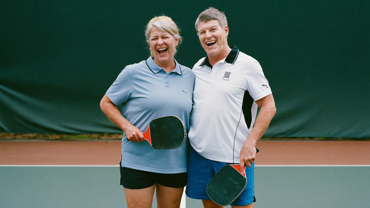 Two people laughing together on an outdoor pickleball court